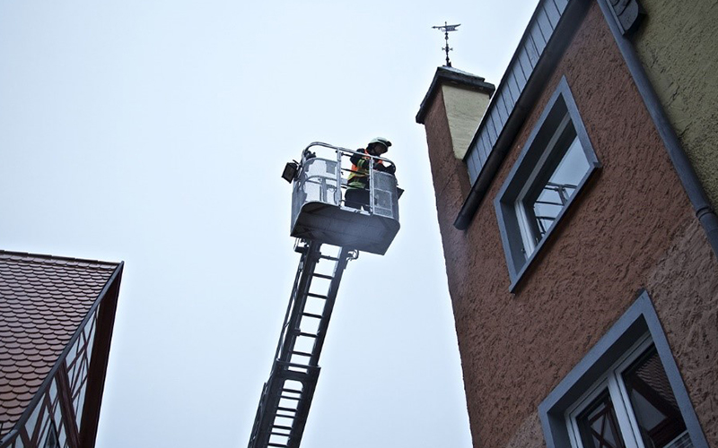 Firefighter on a ladder being raised to the top of a residential building.