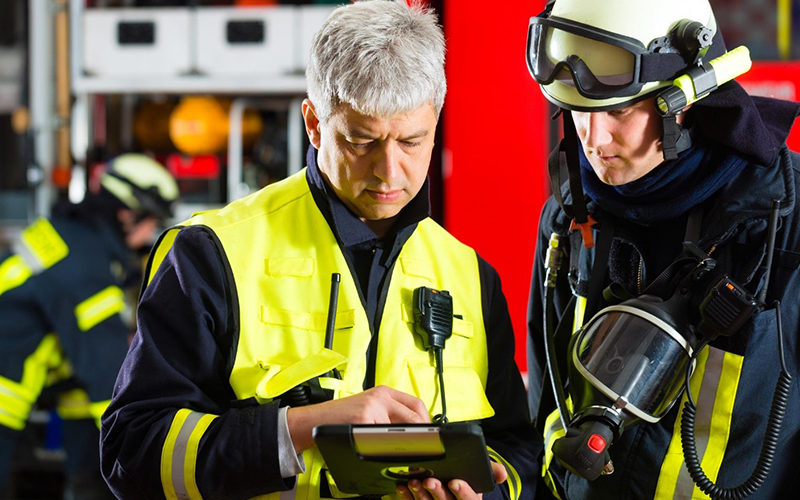 Two firefighters in a firestation, reviewing data on a tablet.