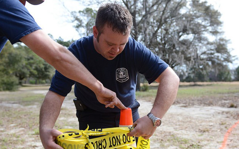 Law enforcement officer outdoors setting up "do not cross" yellow tape.